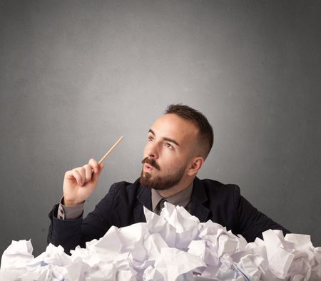 Young businessman sitting behind crumpled paper with grey background