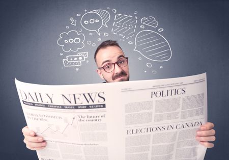 Puzzled young businessman reading daily newspaper with speech bubbles above his head