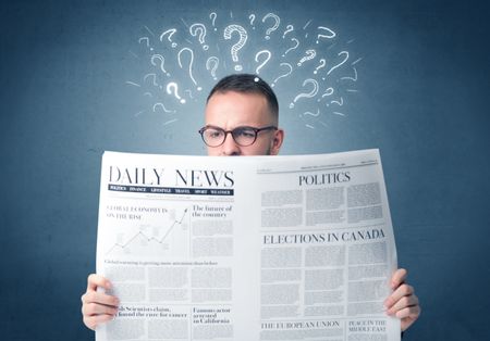 Young confused businessman reading daily newspaper with question marks above his head