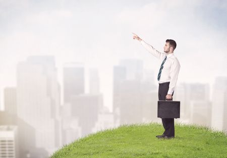 A cheerful caucasian elegant sales manager standing in small green grass in front of faded city landscape, tall buildings concept.