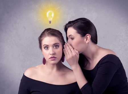 A young girl has an idea illustrated with a drawn glowing light bulb above the head, while a friend whispers a secret in her ear concept.