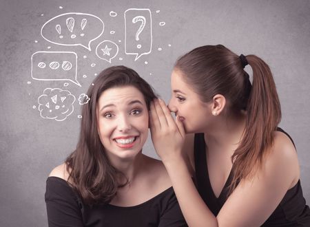 Two girls chatting and sharing their secrets concept with drawn chat bubbles on the background urban wall.