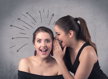 A cute teen caucasian girl telling secret things to her girlfriend dressed in black dress concept with drawn lines, curves, spirals on grey wall background.