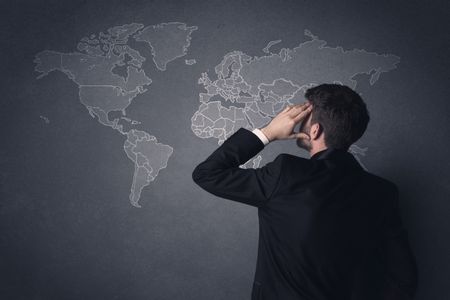 Young businessman in black suit standing in front of a black world map 