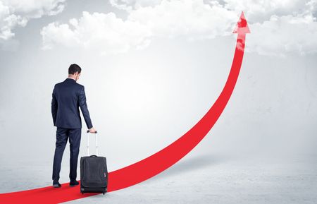 Young businessman with back leaving on the red arrow carpet to the skies with luggage on his hand
