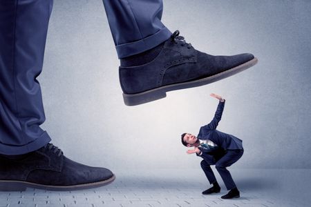 Young handsome businessman getting crushed by a big formal shoe
