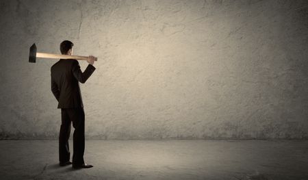 Business man standing in front of a grungy copyspace wall with a hammer