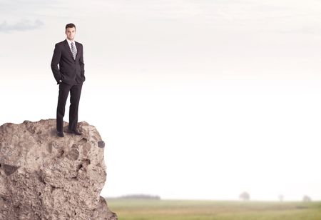 A successful good looking business person standing on top of a high cliff above country landscape with clear white sky concept