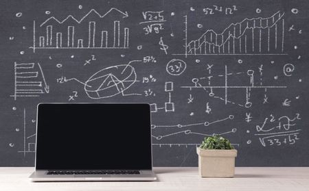 An elegant office desktop with portable laptop and drawn pie charts, graphs, numbers in the background concept