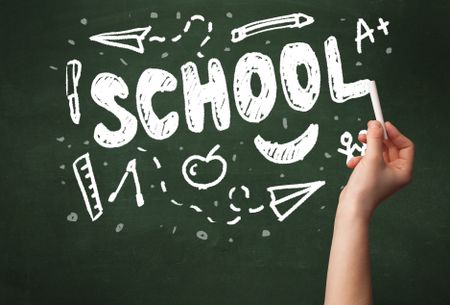 A teacher writing school, drawing children things on clean green chalkboard by hand