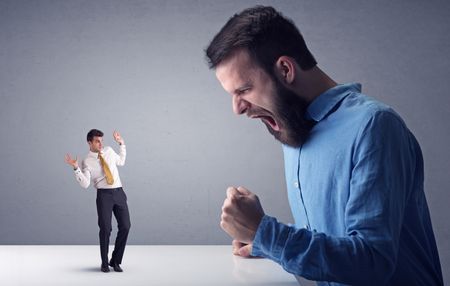 Young professional businessman being angry with an other miniature businessman in front of a grey background