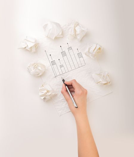 Female hand next to a few crumpled paper balls drawing a progress chart