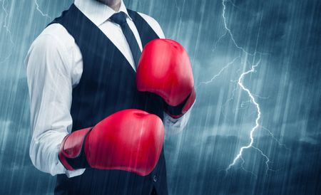 A dangerous sales person getting ready for a fight concept with red boxing gloves and thunder lightning in background.