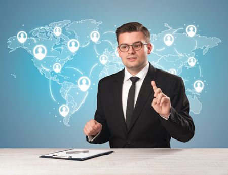 Young handsome businessman sitting at a desk with a blue world map behind him