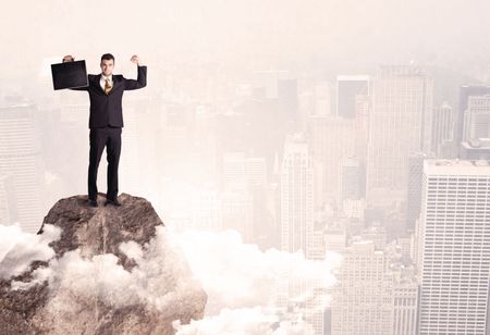 An elegant professional business male standing on top of a high cliff above the clouds looking at the city concept