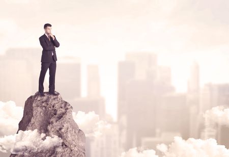 A professional winner business person standing on a dangerous mountain top above the city scape with clouds concept