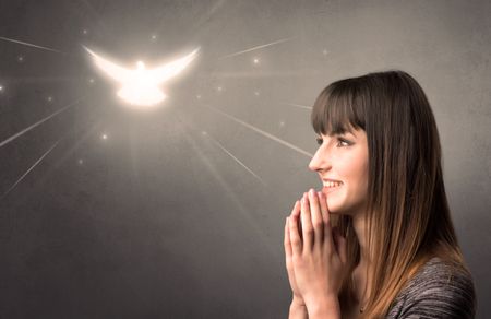 Young woman praying on a grey background with a sparkling bird above her