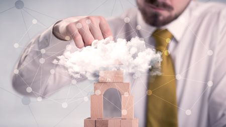 Young handsome businessman using wooden building blocks behind cloud concept