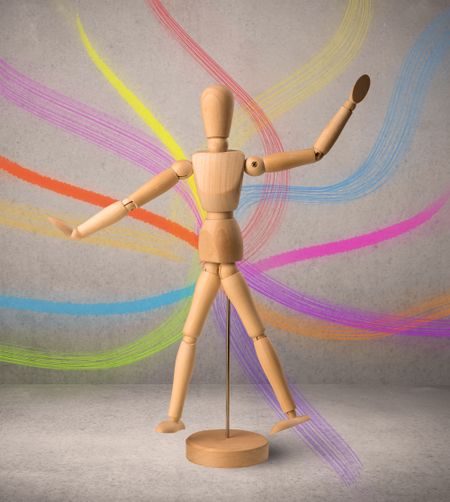 Wooden mannequin posed in front of a greyish background with colorful lines behind it
