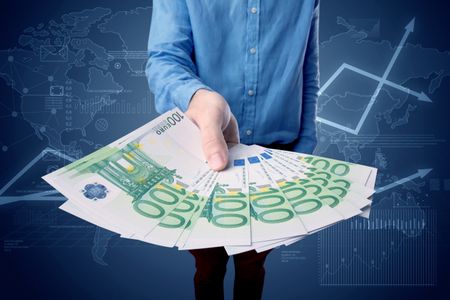 Young businessman holding large amount of bills with blue charts in the background