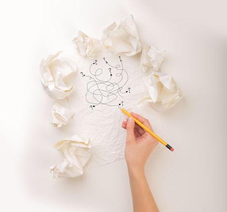 Female hand next to a few crumpled paper balls drawing random scribbles 