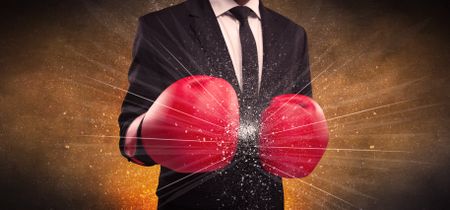 A successful powerful business person in red boxing gloves concept with illustrated power lines and pieces falling apart in front of explosion.