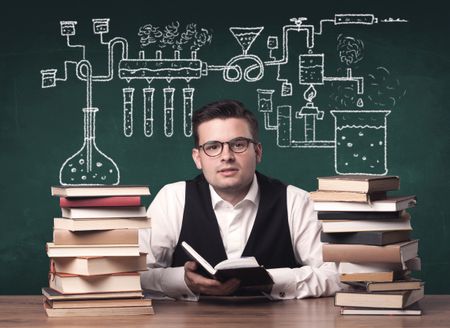 A young chemistry teacher in the middle of a chemical process explanation with tubes, reactions drawn on the blackboard back to school concept.