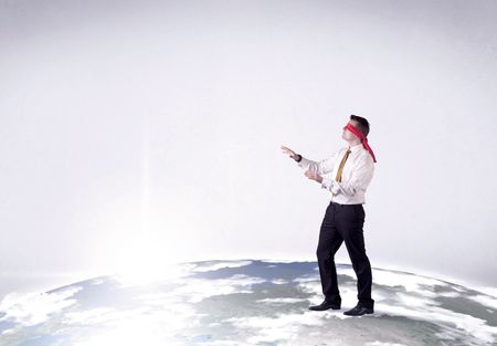 Young blindfolded businessman steps on a realistic globe