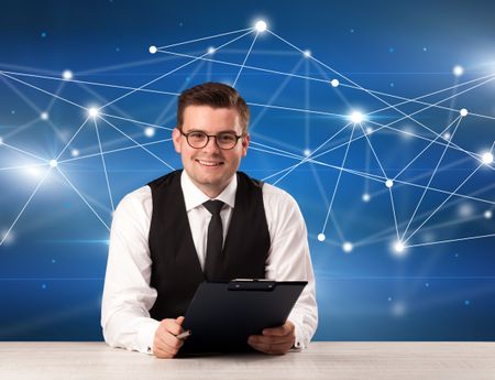 Young handsome businessman sitting at a desk with a blue connection graphic behnid him 
