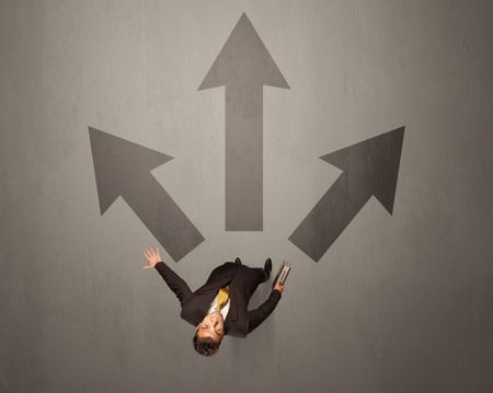 Young contemplating businessman stands in front of brown arrows