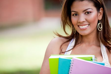 Female student holding notebooks outdoors and smiling