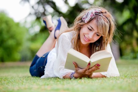 Woman lying on the grass reading a book - outdoors