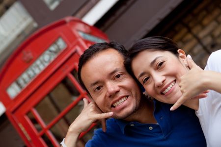 Couple standing in front of a telephone box in London doing a call me gesture