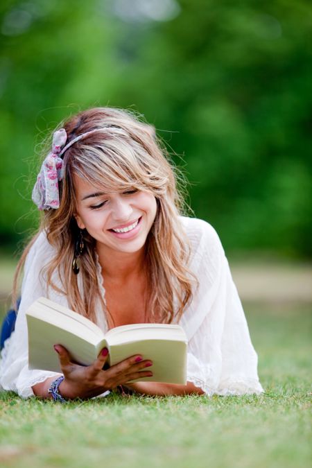 Woman lying on the grass reading a book ? outdoors