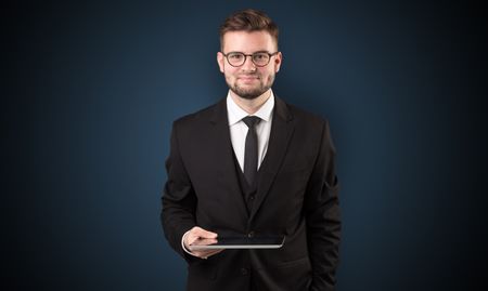Handsome spectacled businessman holding a tablet with dark background
