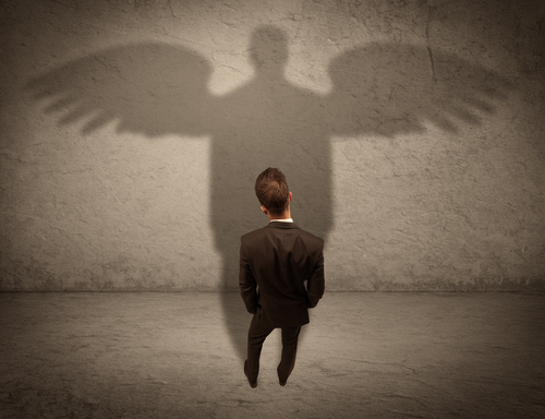 A successful businessman holding a briefcase is giving thumbs up for his angel shadow in front of a wall concept