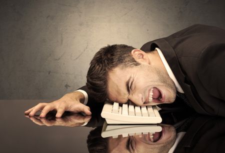 A sad and depressed office worker resting his head on a keyboard while shouting in front of a grey grungy wall background
