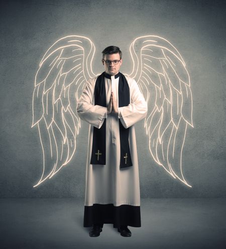 A young male priest with drawn large angel wings standing with the holy bible in his hands concept.