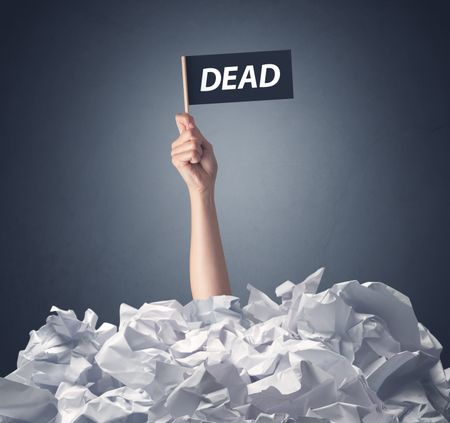 Female hand emerging from crumpled paper pile holding a black flag with dead written on it