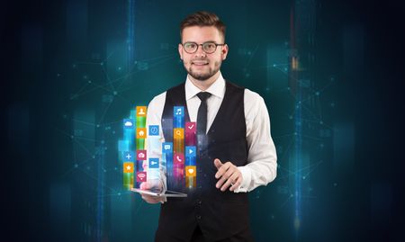 Elegant businessman holding tablet with hologram application icons and symbols above
