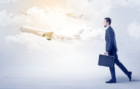Elegant businessman going somewhere with briefcase and airplane on the background
