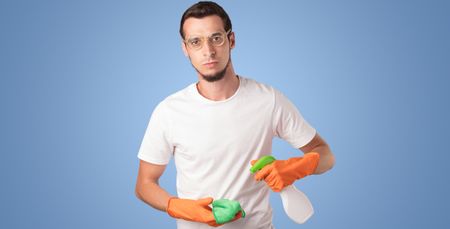 Housekeeper with cleaning product and equipment in front of a blue empty wall
