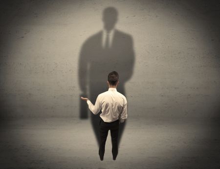 A young beginner salesman standing in front of a wall, facing his shadow as his boss or a successful businessman he lloks up to concept