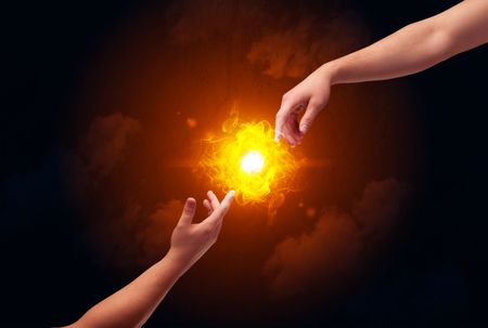 Two naked male hands about to touch, lighting a bright flame with smoke in red sky background concept