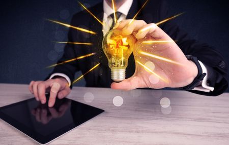 A male business person holding an electric light bulb in his hand with beam rays illustration concept.