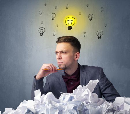 Young businessman sitting behind crumpled paper with lightbulbs above his head