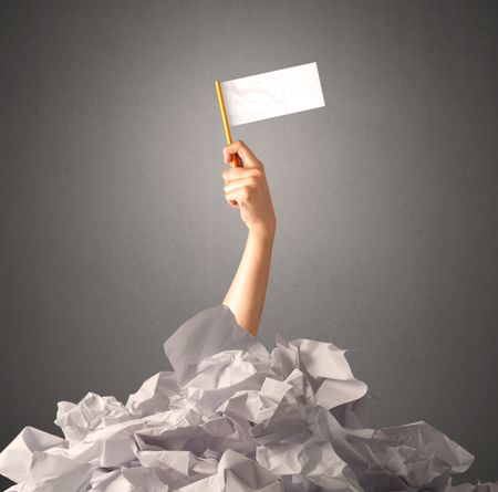 Female hand emerging from crumpled paper pile holding a white blank flag 