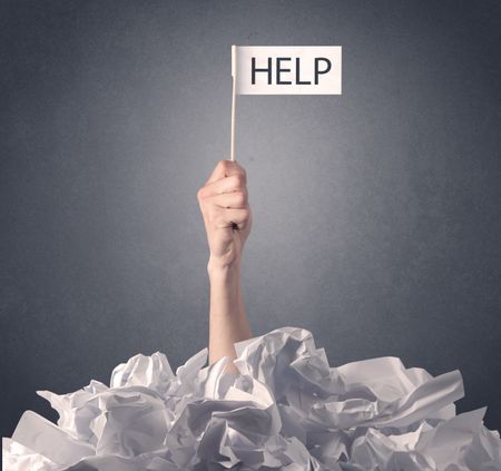 Female hand emerging from crumpled paper pile holding help sign