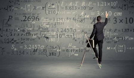 A businessman in elegant suit standing on a small ladder and writing numbers, calculating on grey wall background