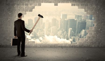 Business man hitting wall with hammer on city view background
